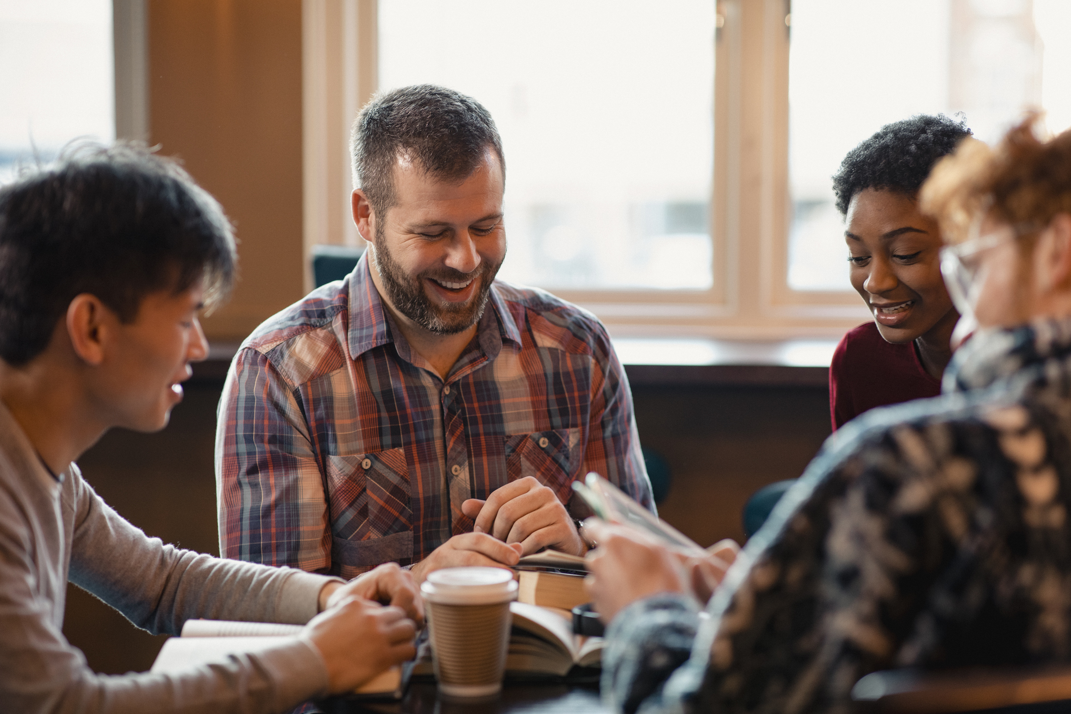 Small group of people with a mixed age range sitting at a table, discussing and reading books together